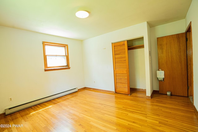 unfurnished bedroom with light wood-type flooring, a closet, and a baseboard heating unit