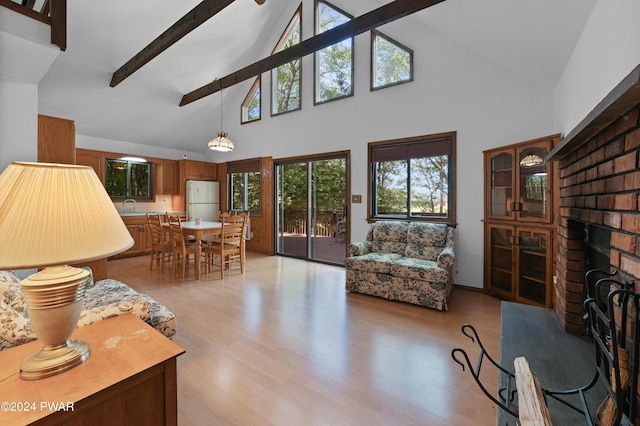 living room with high vaulted ceiling, sink, light hardwood / wood-style flooring, a brick fireplace, and beam ceiling