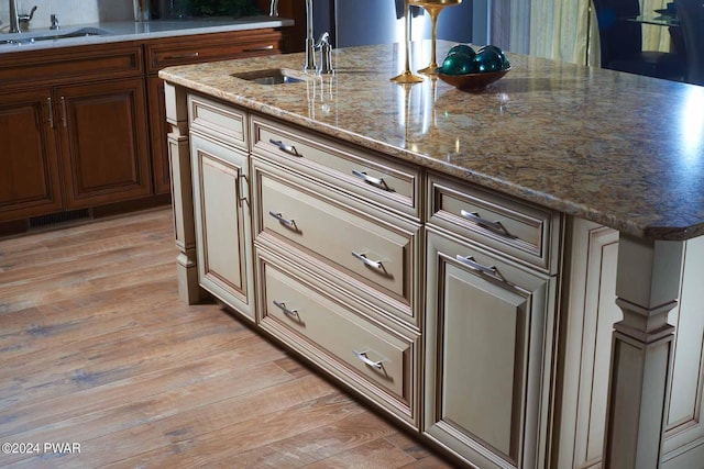 kitchen with light stone counters, light hardwood / wood-style floors, sink, and a kitchen island with sink