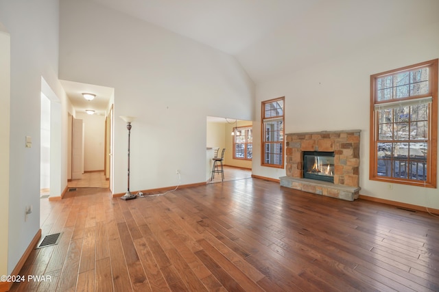 unfurnished living room featuring wood-type flooring, high vaulted ceiling, a stone fireplace, and a wealth of natural light