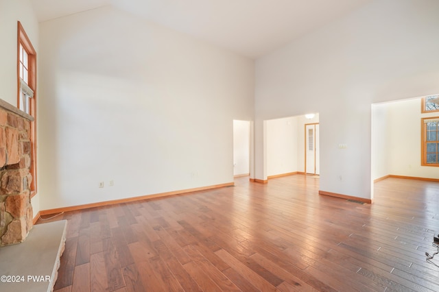 unfurnished living room featuring a stone fireplace, high vaulted ceiling, and hardwood / wood-style flooring