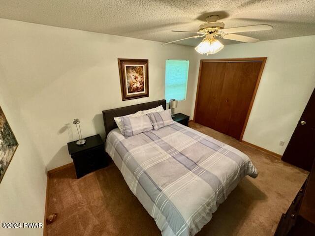 carpeted bedroom with ceiling fan, a closet, and a textured ceiling