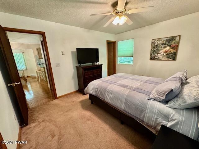 bedroom featuring ceiling fan, light colored carpet, and a textured ceiling