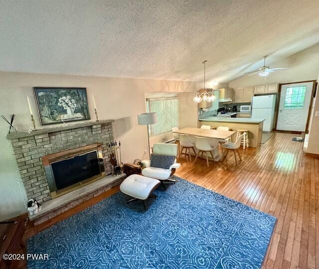 living room with ceiling fan with notable chandelier, light wood-type flooring, a textured ceiling, and a brick fireplace