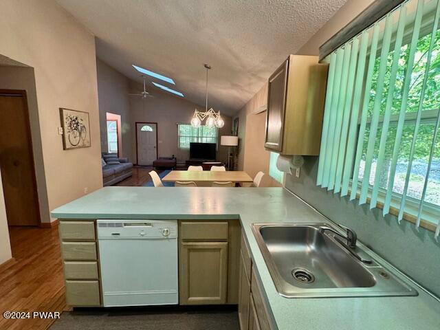 kitchen featuring kitchen peninsula, a textured ceiling, white dishwasher, lofted ceiling with skylight, and sink