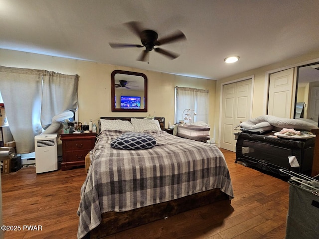 bedroom featuring wood finished floors, baseboard heating, a ceiling fan, and two closets