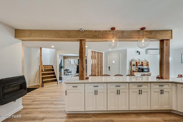 kitchen with heating unit, decorative light fixtures, a wall mounted AC, white cabinets, and light hardwood / wood-style floors