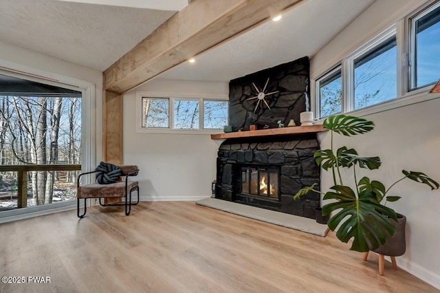 sitting room featuring a stone fireplace, wood-type flooring, beamed ceiling, and plenty of natural light