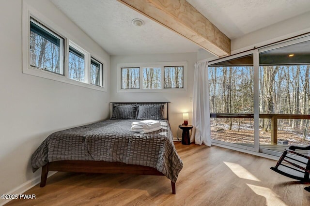 bedroom with beam ceiling, light hardwood / wood-style flooring, and a textured ceiling