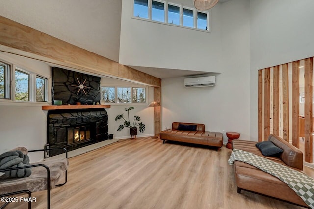 sitting room featuring a stone fireplace, hardwood / wood-style floors, a high ceiling, and an AC wall unit