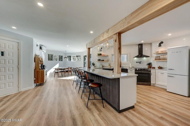 kitchen featuring white cabinetry, a center island, white refrigerator, stainless steel electric range oven, and wall chimney exhaust hood