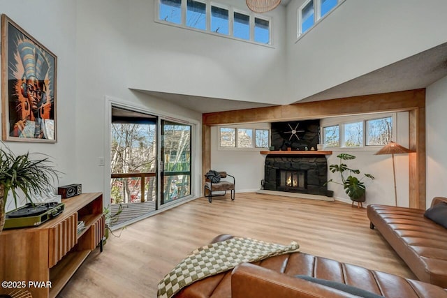 living room with a stone fireplace, a towering ceiling, and light wood-type flooring