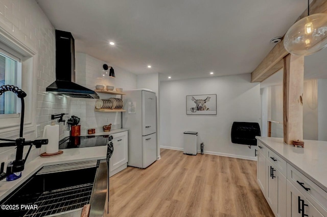 kitchen featuring white cabinetry, backsplash, light hardwood / wood-style floors, decorative light fixtures, and wall chimney exhaust hood