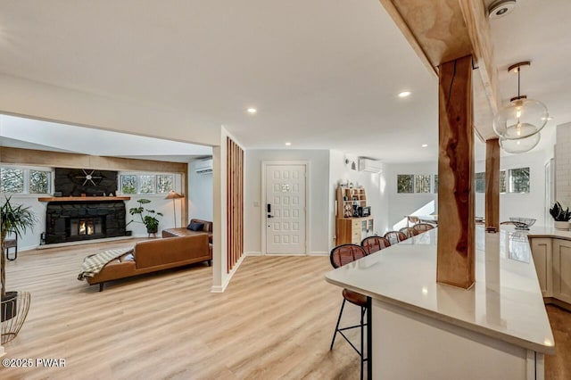 interior space featuring a stone fireplace, a wall mounted AC, and light wood-type flooring