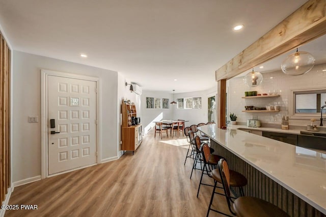 kitchen with a kitchen bar, light hardwood / wood-style flooring, pendant lighting, light stone countertops, and backsplash