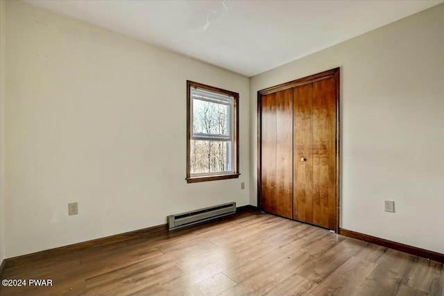 unfurnished bedroom with a closet, baseboard heating, and light hardwood / wood-style floors