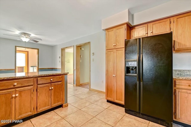 kitchen featuring ceiling fan, black fridge with ice dispenser, light tile patterned floors, and light stone counters