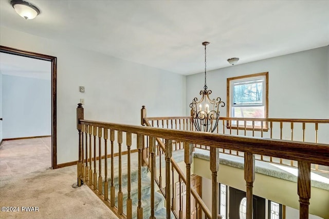 hall with light carpet and an inviting chandelier