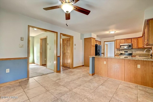 kitchen with sink, appliances with stainless steel finishes, tasteful backsplash, light stone counters, and kitchen peninsula