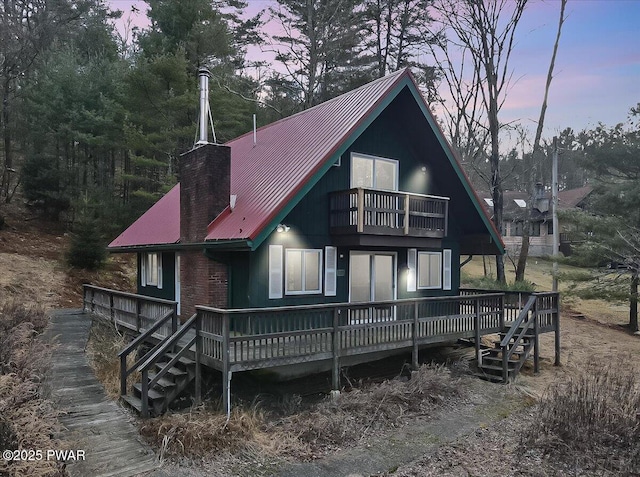 back house at dusk with a balcony and a wooden deck