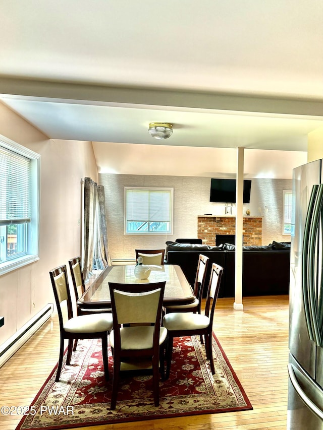 129 Skyview Rd, Dingmans Ferry, PA 18328 - dining area featuring baseboard heating, a brick fireplace, light wood-style floors, healthy amount of natural light, and beamed ceiling