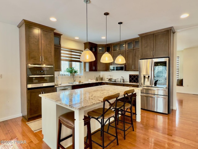 kitchen featuring glass insert cabinets, light wood finished floors, a kitchen island, and appliances with stainless steel finishes