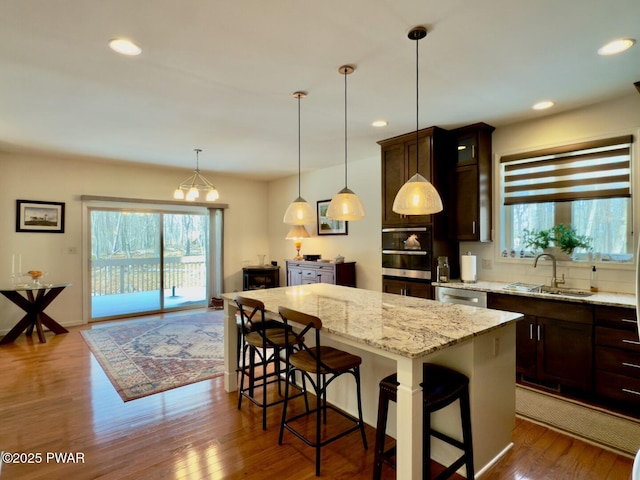 kitchen featuring dark brown cabinetry, dark wood-style floors, a kitchen island, stainless steel appliances, and a sink