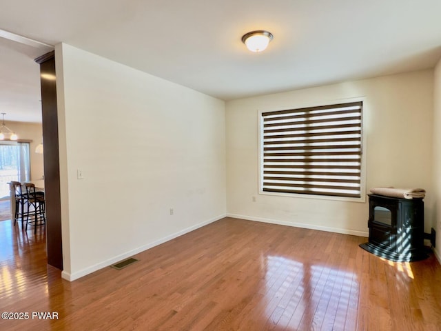 empty room with a wood stove, wood-type flooring, visible vents, and baseboards