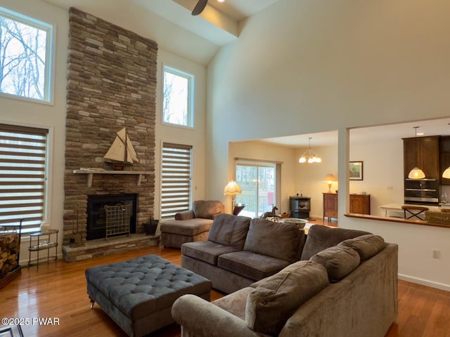 living room featuring a fireplace, a high ceiling, wood finished floors, a chandelier, and baseboards