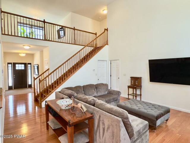 living room with baseboards, stairway, a towering ceiling, and wood finished floors