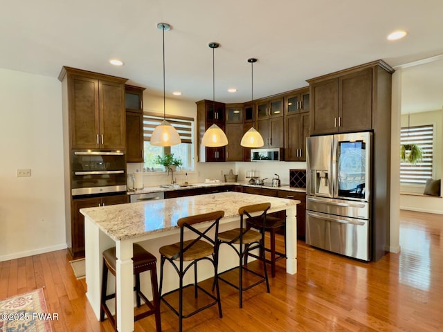 kitchen with light wood-style flooring, a center island, stainless steel appliances, dark brown cabinets, and a sink