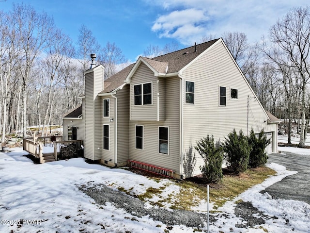 snow covered house featuring a deck, roof with shingles, and a chimney