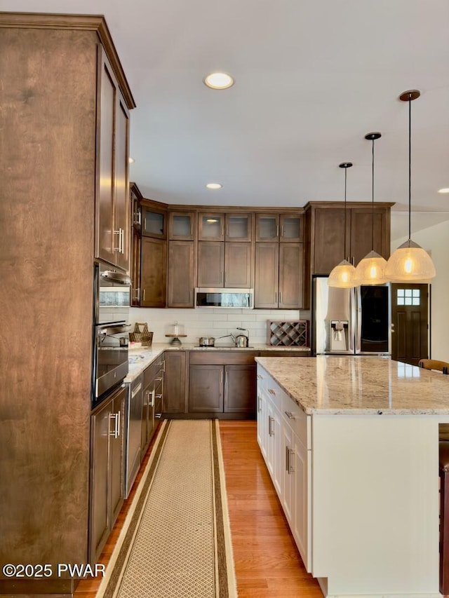 kitchen with appliances with stainless steel finishes, a center island, light wood finished floors, glass insert cabinets, and pendant lighting