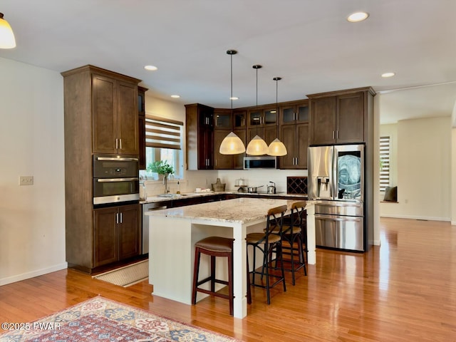 kitchen with dark brown cabinetry, a kitchen island, stainless steel appliances, light wood-type flooring, and a sink