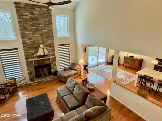 living room featuring a healthy amount of sunlight, ceiling fan, wood finished floors, and a stone fireplace