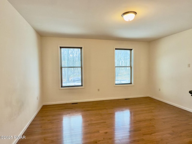 unfurnished room featuring a healthy amount of sunlight, baseboards, and wood finished floors