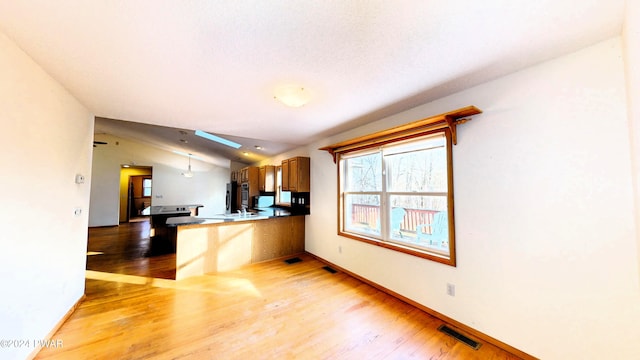 kitchen with a breakfast bar area, kitchen peninsula, lofted ceiling with skylight, and light hardwood / wood-style flooring