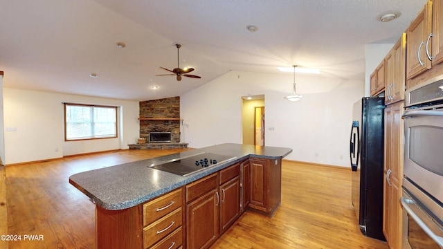 kitchen with a center island, a stone fireplace, hanging light fixtures, and black appliances