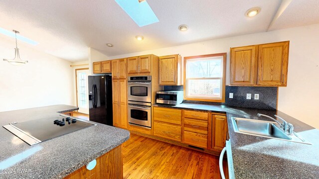 kitchen with a skylight, stainless steel appliances, sink, pendant lighting, and hardwood / wood-style floors