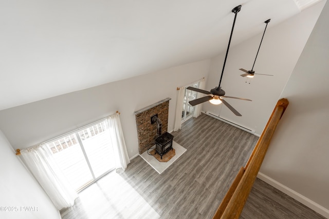 detailed view of a wood stove, a baseboard radiator, a ceiling fan, wood finished floors, and baseboards