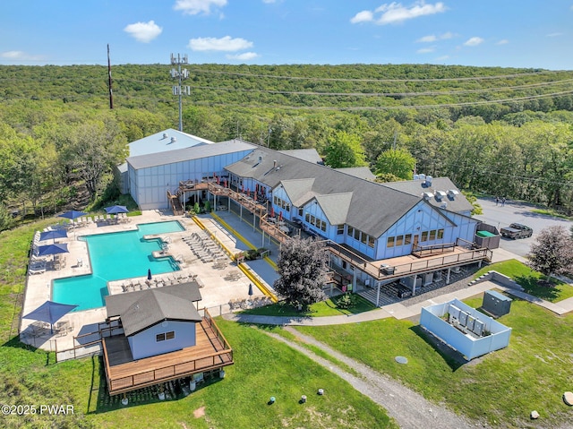 aerial view of property and surrounding area with a heavily wooded area and a pool area
