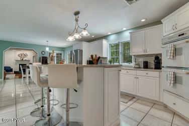 3043 Hemlock Rd, Stroudsburg, PA 18360 - kitchen featuring freestanding refrigerator, double oven, light tile patterned floors, white cabinets, and a kitchen island