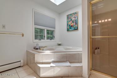 3043 Hemlock Rd, Stroudsburg, PA 18360 - bathroom featuring a baseboard heating unit, tile patterned floors, a bath, a stall shower, and a skylight