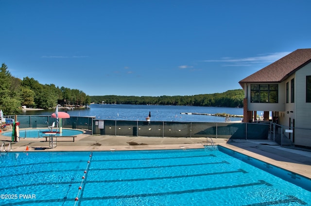 pool with a water view, a view of trees, fence, and a patio