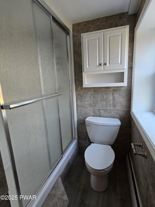 bathroom with toilet, tile walls, a shower with shower door, and a baseboard heating unit