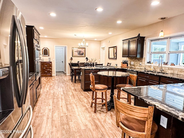 kitchen featuring light wood-type flooring, backsplash, stainless steel appliances, sink, and hanging light fixtures