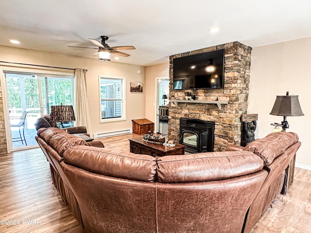 living room with light hardwood / wood-style floors, a wood stove, ceiling fan, and a baseboard heating unit