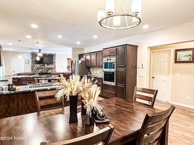 dining room with a fireplace, ceiling fan with notable chandelier, and light hardwood / wood-style flooring