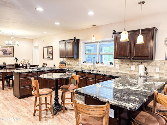 kitchen with sink, a kitchen breakfast bar, tasteful backsplash, dark stone counters, and decorative light fixtures