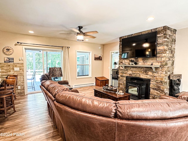 living room with light hardwood / wood-style flooring, a wood stove, ceiling fan, and a baseboard heating unit